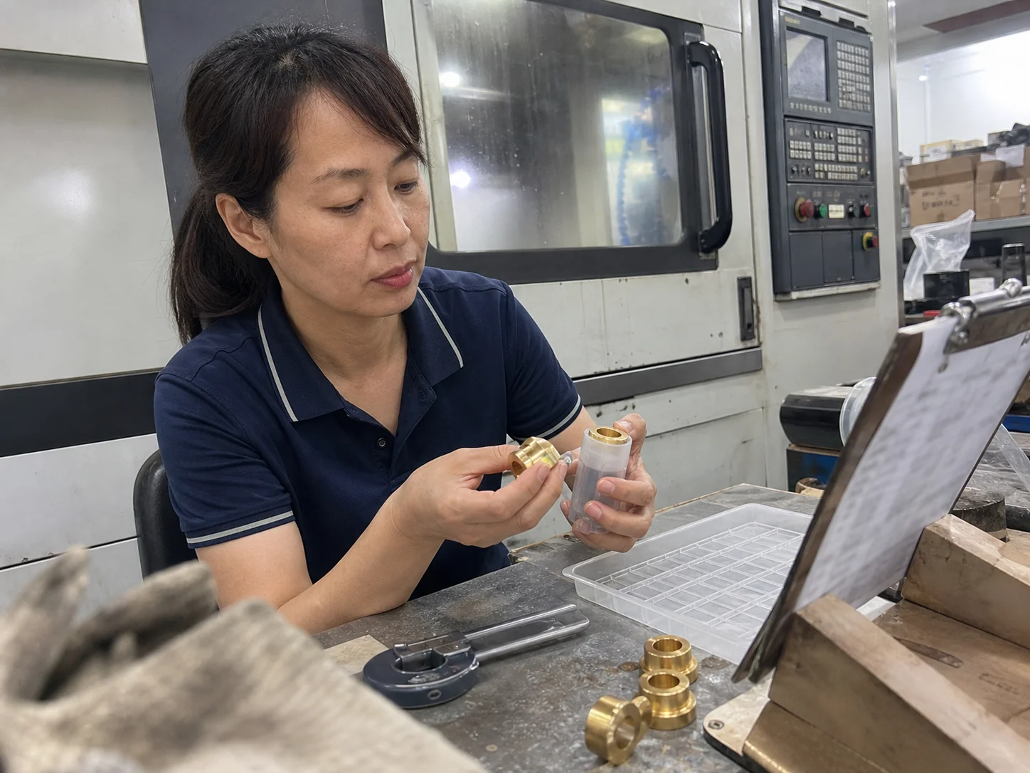 女性质量检验员在工艺卡旁核对法兰铜嵌件与剖开塑胶试装柱